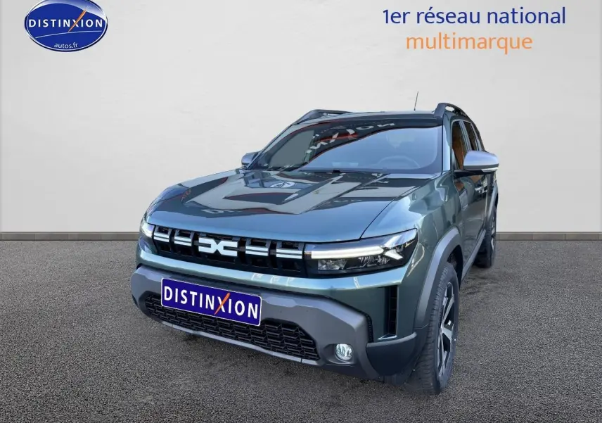 Dacia Duster 2025 vert cèdre en 3/4 avant droit, avec jantes alu et barres de toit visibles.