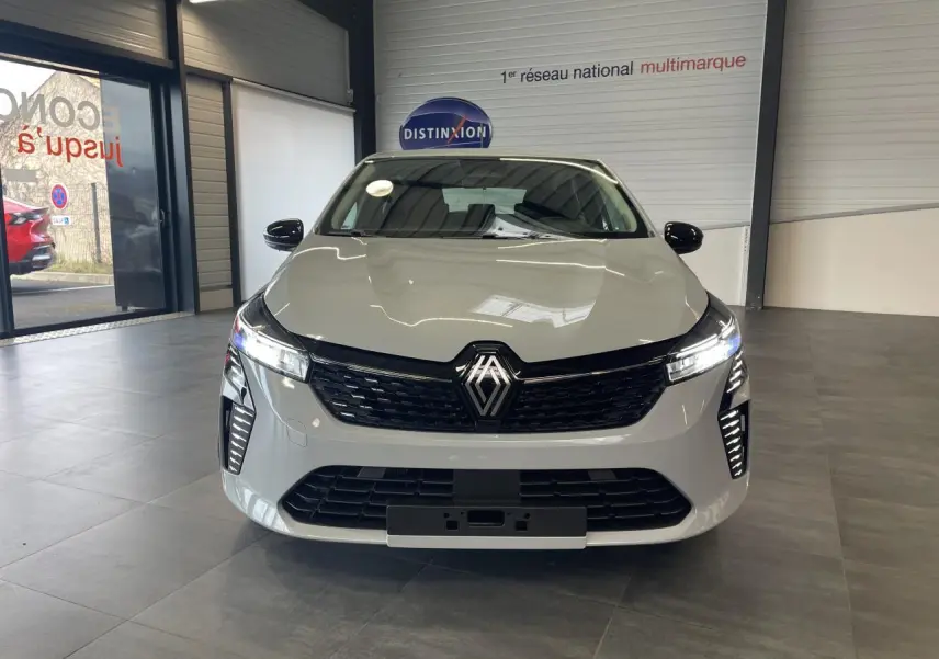Renault Clio 1.5 Blue dCi 2025 en gris Rafale vue de face en intérieur, avec calandre noire et feux LED allumés.