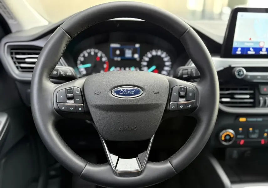 Vue rapprochée du volant en cuir multifonctions du Ford Kuga 2024 avec tableau de bord et écran GPS tactile en arrière-plan.
