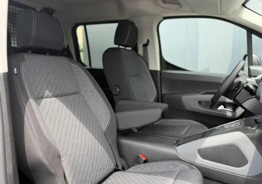 Vue intérieure côté conducteur du Peugeot Rifter 2026, sièges tissu gris avec accoudoir central et volant multifonction.