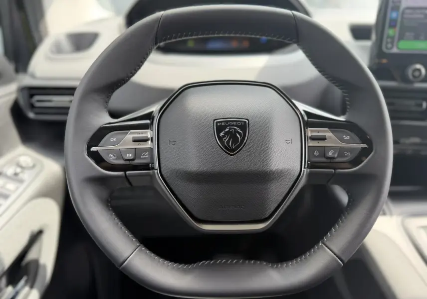 Vue rapprochée du volant cuir noir du Peugeot Rifter 2026 avec commandes multifonctions et logo lion central.