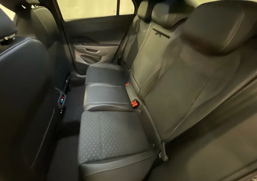 Vue intérieure arrière droite des sièges tissu noirs du Volkswagen T-Roc 2026 avec accoudoir central et ceintures rouges.