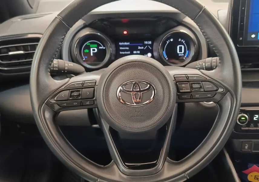Vue rapprochée du volant cuir noir de la Toyota Yaris Hybride 116h 2022 avec tableau de bord numérique allumé.