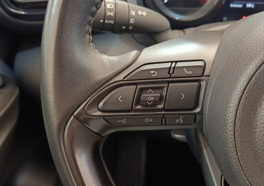 Gros plan sur les commandes multifonctions du volant cuir noir de la Toyota Yaris Hybride 116h Collection 2022.