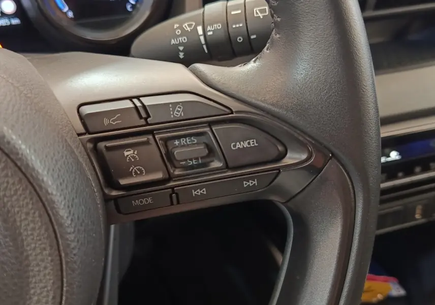 Gros plan sur le côté droit du volant cuir noir de la Toyota Yaris Hybride 116h avec commandes multifonctions intégrées.