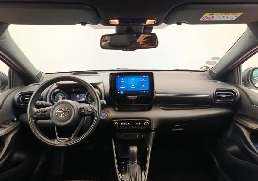 Vue intérieure frontale du tableau de bord noir de la Toyota Yaris Hybride 116h avec écran tactile central et volant multifonctions.
