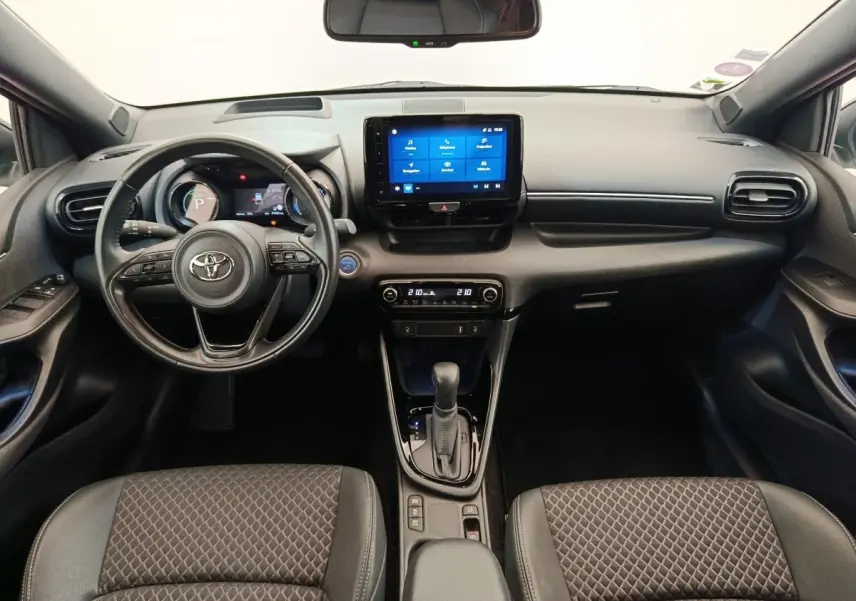 Vue intérieure avant de la Toyota Yaris Hybride 116h 2022, tableau de bord noir avec écran tactile central et volant cuir.