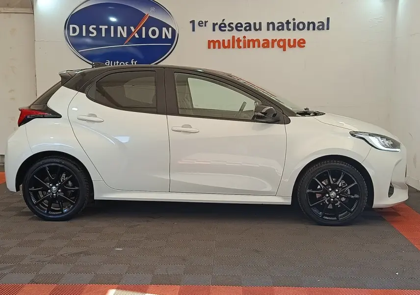 Profil droit d'une Toyota Yaris hybride blanche 2022 avec jantes noires et toit noir, en intérieur showroom.