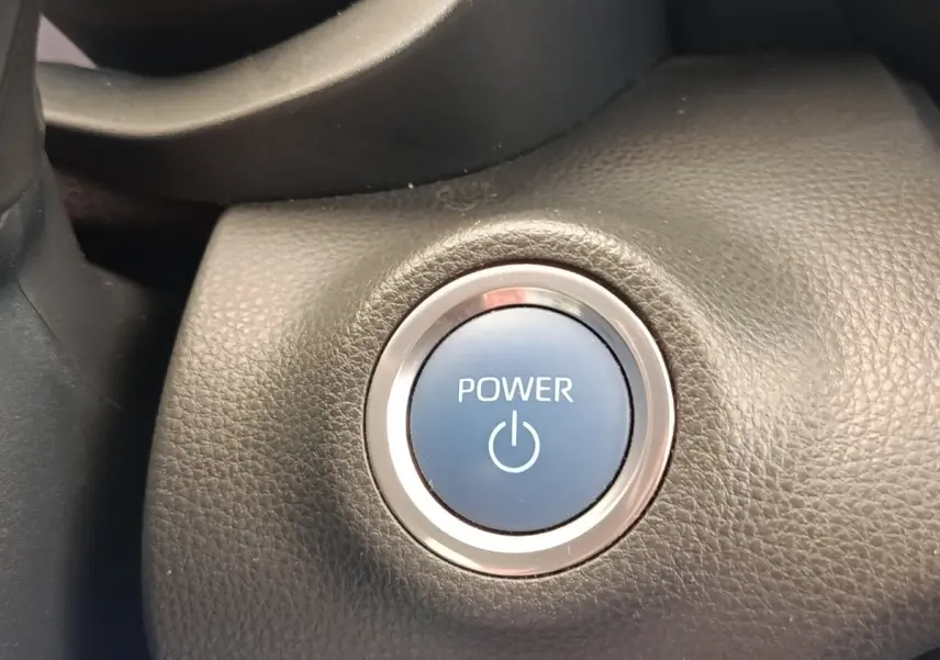 Gros plan sur le bouton démarrage Power bleu entouré de chrome dans l’habitacle noir d’une Toyota Yaris hybride 2022.