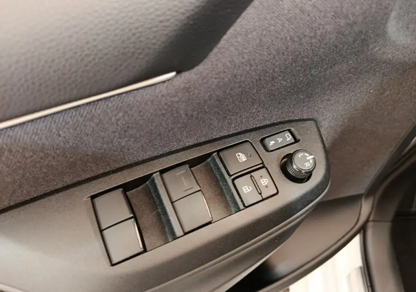 Détail des commandes de lève-vitres et réglage des rétroviseurs côté conducteur dans une Toyota Yaris Hybride blanche 2022.
