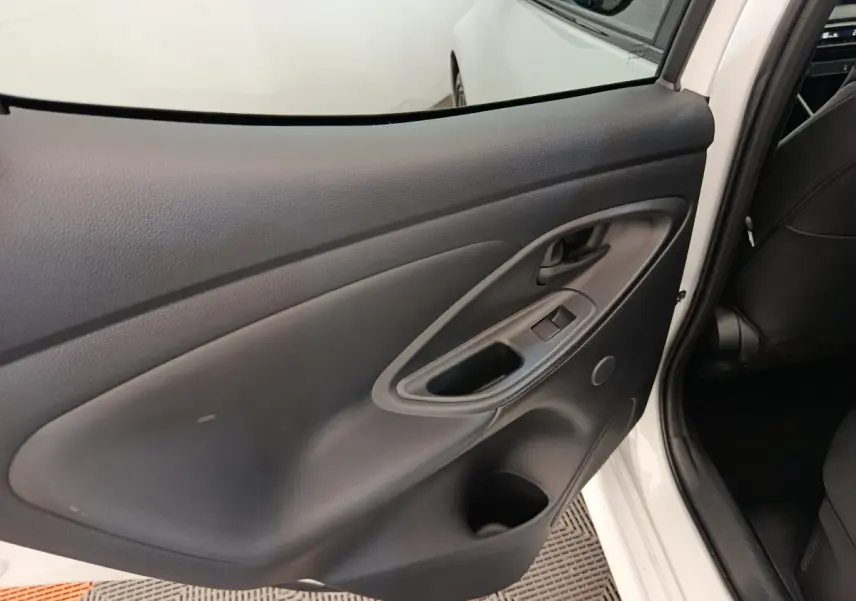 Vue intérieure de la porte arrière gauche noire d'une Toyota Yaris hybride blanche, avec poignée et commandes de fenêtre.