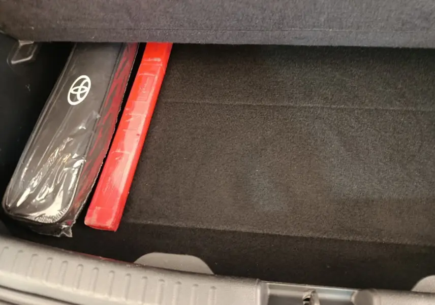 Coffre ouvert de Toyota Yaris Hybride blanc, vue plongeante sur tapis noir avec kit de sécurité rangé sur le côté.
