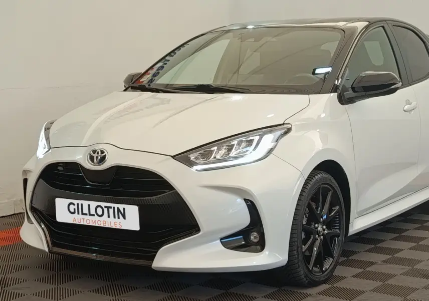 Toyota Yaris Hybride 116h blanc vue 3/4 avant droit avec calandre noire et jantes alliage noires.