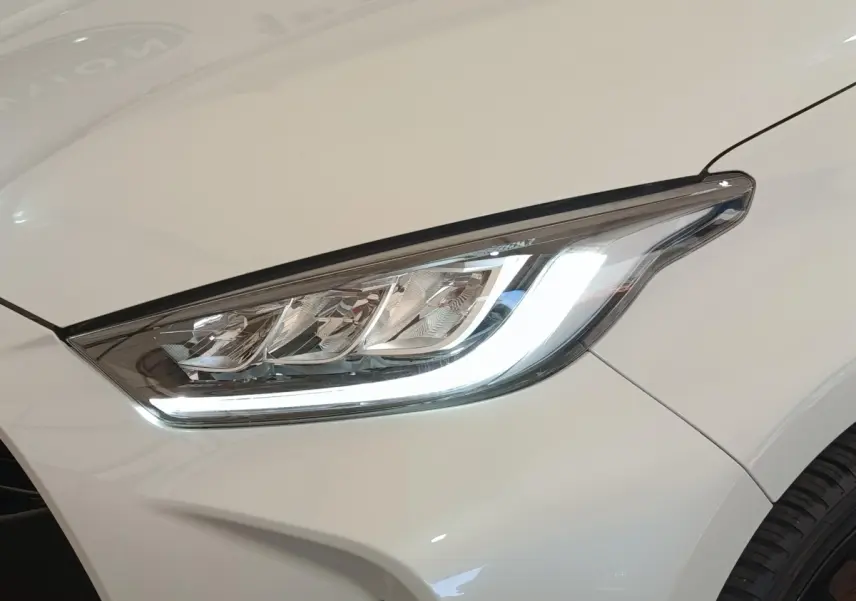 Gros plan sur le phare avant droit LED d'une Toyota Yaris Hybride blanche, soulignant ses lignes modernes et précises.