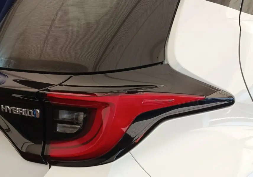 Gros plan sur le feu arrière droit rouge et noir d’une Toyota Yaris Hybride blanche, avec logo Hybrid visible.
