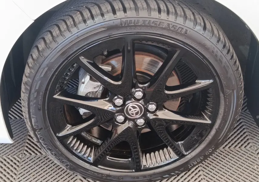 Gros plan sur la jante noire brillante et le pneu multisaison d’une Toyota Yaris blanche hybride 2022.