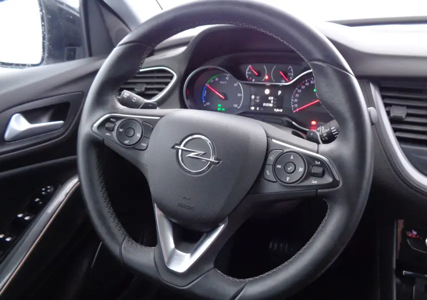 Vue rapprochée du volant en cuir noir de l'Opel Grandland X hybride, avec commandes intégrées et tableau de bord digital.