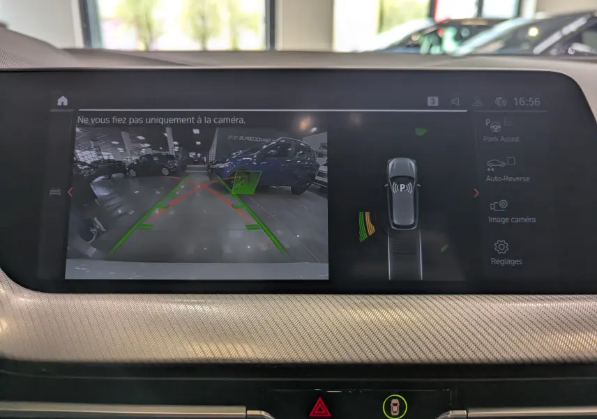 Affichage de la caméra de recul sur BMW Série 1 blanche, avec lignes de guidage et alertes de stationnement visibles.