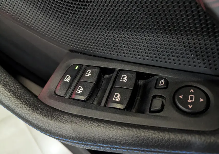 Gros plan sur les commandes électriques des vitres et rétroviseurs côté conducteur de la BMW Série 1 F40 blanc alpin.