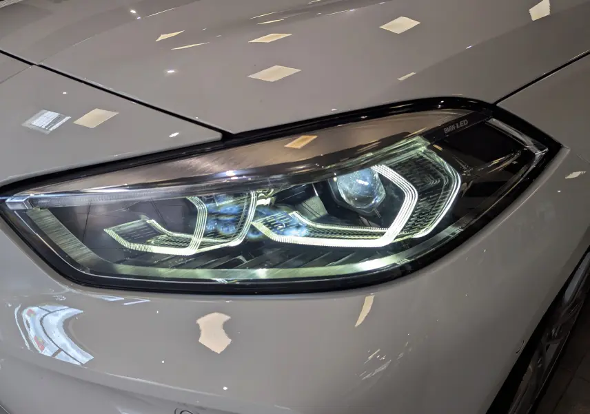 Gros plan sur le phare avant droit blanc alpin d'une BMW Série 1 F40 18d 2023 avec éclairage LED distinctif.