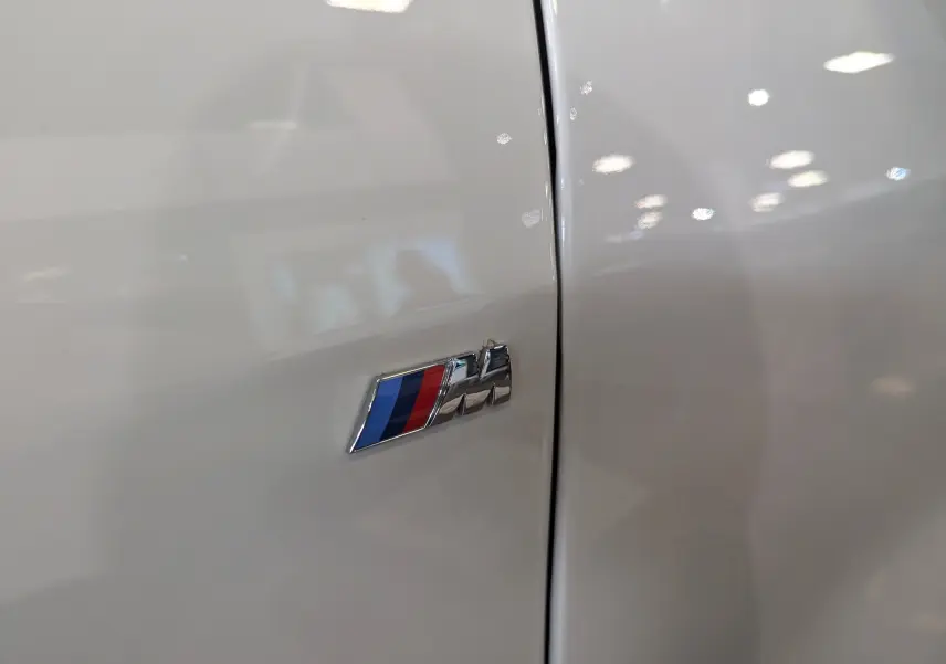 Gros plan sur l'emblème M Sport bleu, rouge et violet sur la carrosserie blanche alpin d'une BMW Série 1 F40.