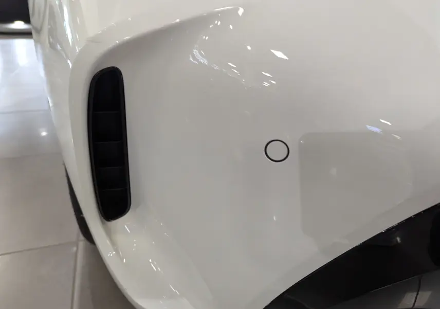 Détail du pare-chocs avant blanc alpin d'une BMW Série 1 F40 18d M Sport avec capteur de stationnement et prise d'air noire.