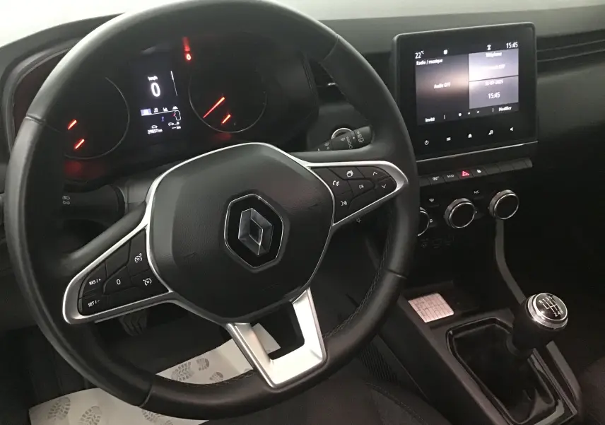 Vue intérieure du volant et tableau de bord d'une Renault Clio V gris platine avec boîte manuelle et écran tactile central.