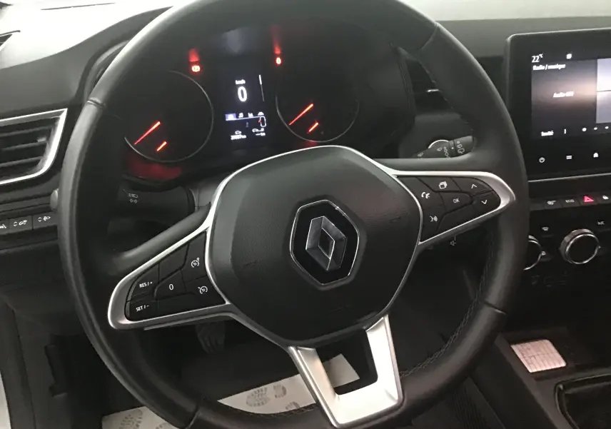 Vue rapprochée du volant noir de la Renault Clio V gris platine avec commandes intégrées et tableau de bord numérique.