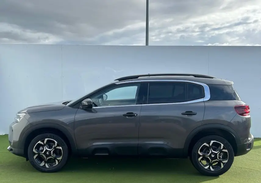 Profil côté gauche d'un Citroën C5 Aircross gris platinium métallisé avec jantes alliage bi-ton et barres de toit noires.
