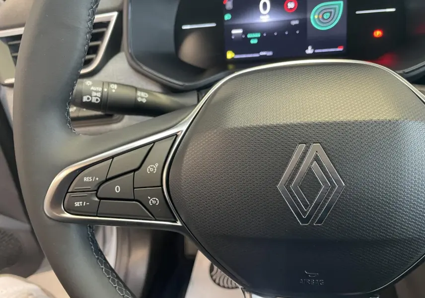 Gros plan sur le volant multifonction noir avec logo Renault chromé et tableau de bord numérique de la Renault Clio 2025.