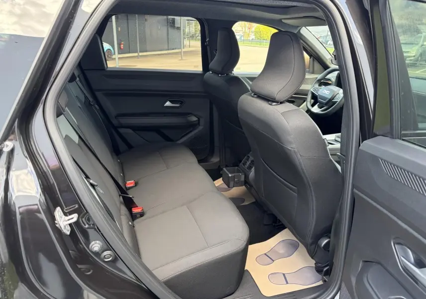 Vue intérieure côté arrière droit du Dacia Bigster noir, montrant la banquette arrière et les sièges avant en tissu noir.