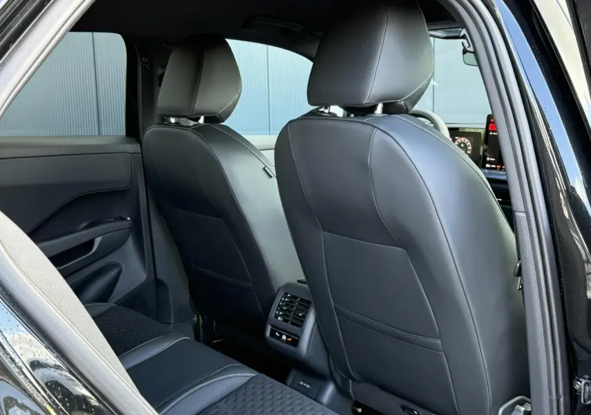 Vue arrière intérieure du Volkswagen T-Roc noir Ébène, montrant les sièges avant en cuir et la console avec ventilation arrière.