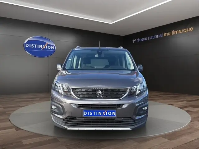 Vue frontale d'un Peugeot Rifter gris foncé 2020 avec calandre chromée et phares LED dans un showroom.