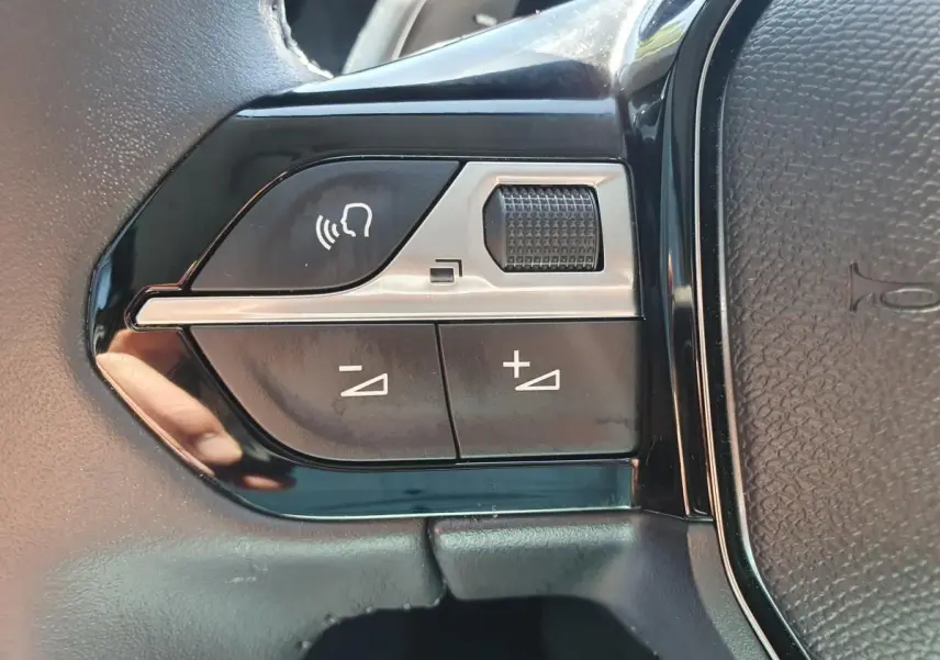 Gros plan sur les commandes de volume vocal et sonore au volant du Peugeot 208 gris Artense, version hybride 2025.