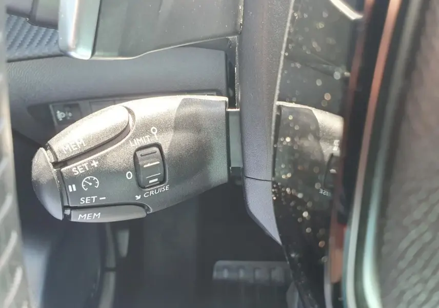 Gros plan sur la commande de régulateur de vitesse à gauche du volant dans une Peugeot 208 gris Artense 2025.
