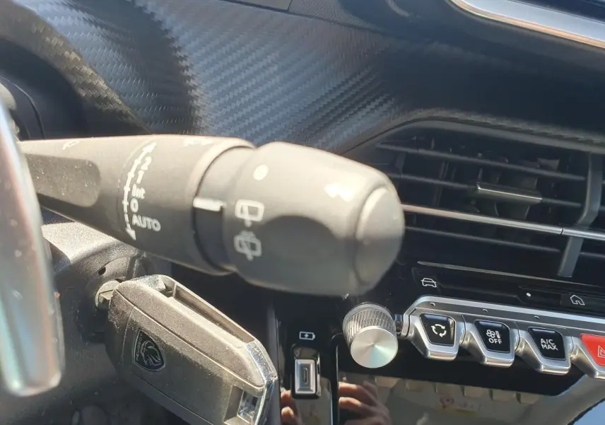 Détail intérieur du tableau de bord de la Peugeot 208 gris Artense, avec commandes d’essuie-glace et boutons de climatisation.