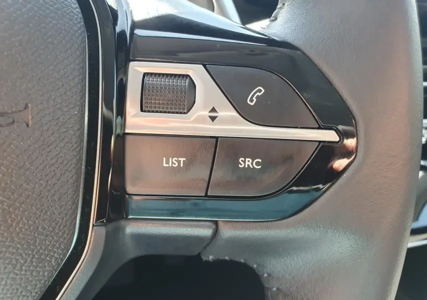 Gros plan sur les commandes gauche du volant noir de la Peugeot 208 1.2 Hybrid 110 gris Artense, boutons appel et audio.