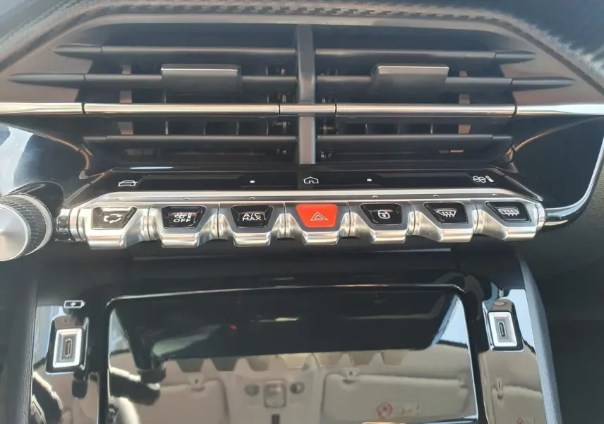 Vue rapprochée de la console centrale de la Peugeot 208 1.2 Hybrid 110, boutons argentés et noir brillant.