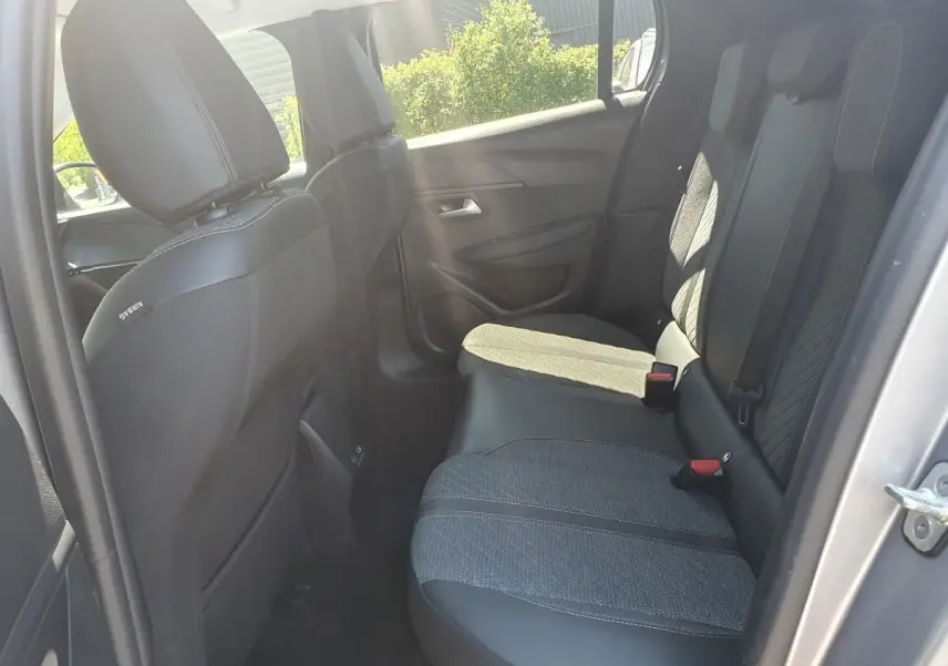 Vue intérieure côté arrière droit de la Peugeot 208 1.2 Hybrid 110 Allure, sièges tissu noir avec surpiqûres grises.