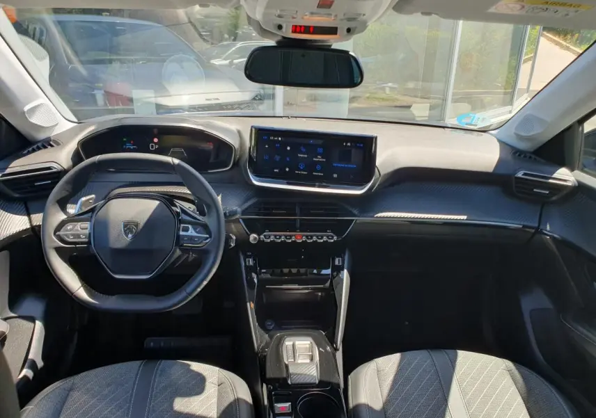 Vue intérieure avant de la Peugeot 208 1.2 Hybrid 110 Allure, tableau de bord moderne avec écran tactile 10'' et volant compact.