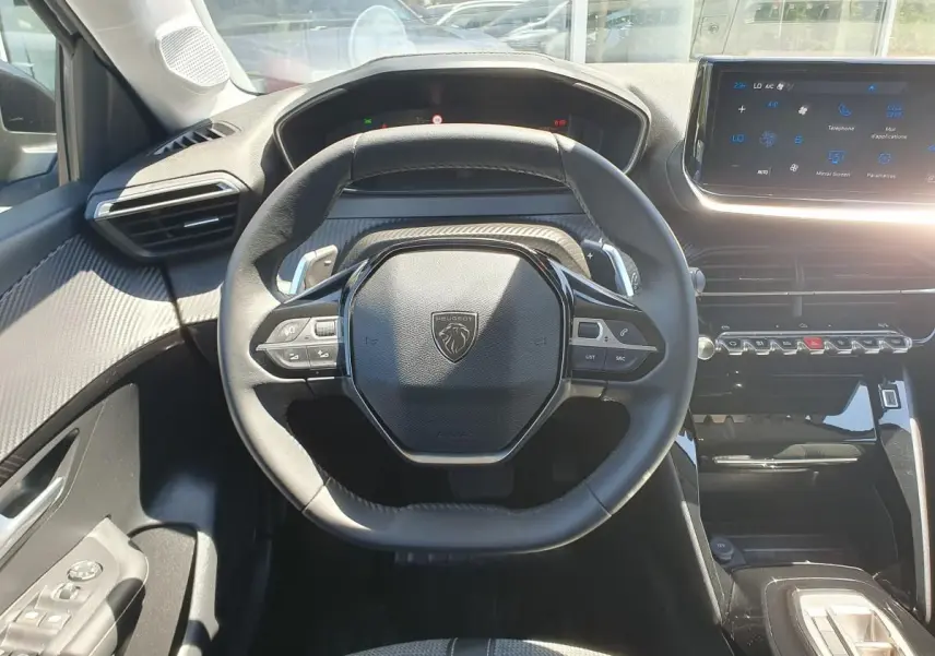 Vue intérieure centrée sur le volant noir de la Peugeot 208 1.2 Hybrid 110 Allure avec tableau de bord et écran tactile.