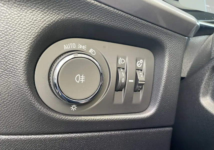 Gros plan sur le bouton de commande des phares et réglages d’éclairage intérieur du tableau de bord noir de l’Opel Mokka 2023.