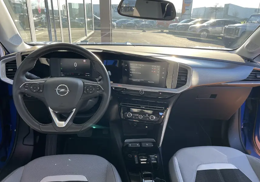 Vue intérieure avant de l'Opel Mokka bleu Voltak 2023, tableau de bord moderne avec écran tactile et volant multifonction.