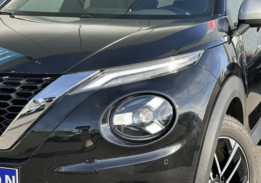 Gros plan sur l'avant droit noir du Nissan Juke 2025, mettant en valeur le phare rond et la calandre chromée.