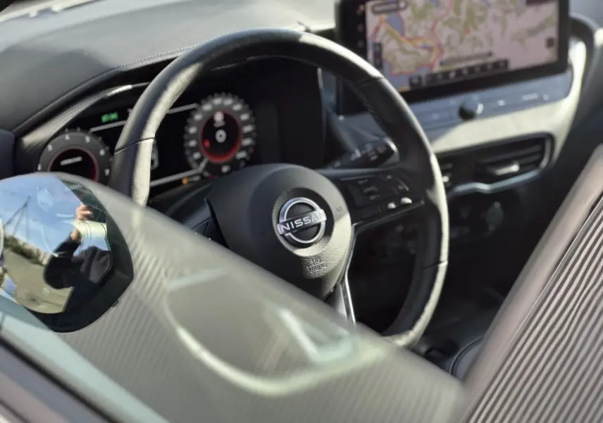 Vue rapprochée de l'intérieur du Nissan Juke 2025, volant en cuir noir avec tableau de bord digital et écran tactile GPS.