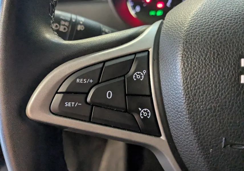 Gros plan sur les commandes de régulateur de vitesse au volant noir du Dacia Duster gris 2023, côté gauche.