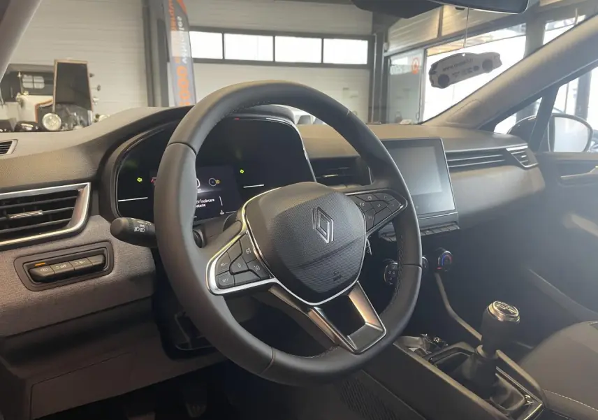 Vue intérieure centrée sur le volant multifonction et la console centrale d'une Renault Clio 2025 noire étoile.