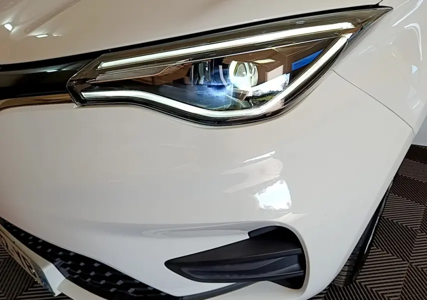 Gros plan sur le phare avant droit blanc de la Renault ZOE Zen R110 avec détails LED et calandre noire.
