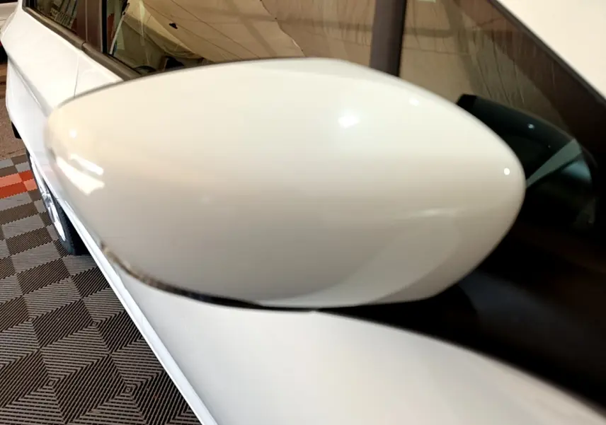 Gros plan sur le rétroviseur droit blanc d'une Renault ZOE Zen R110, avec la portière et vitre arrière visibles.