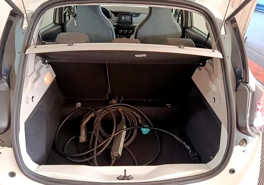Coffre ouvert d’une Renault ZOE blanche vue arrière, avec câble de recharge électrique visible à l’intérieur.